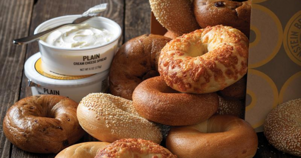 einstein bagels overflowing from an Einstein bagel box with 2 tubs of cream cheese and a knife