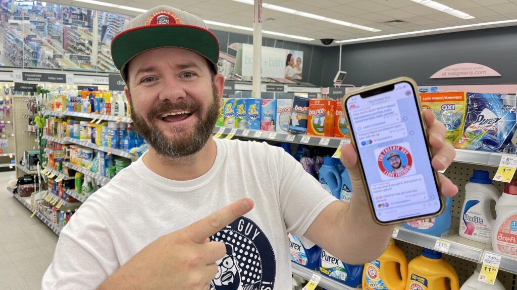the freebie guy standing in a store holding his cell phone pointing to it and on the phone screen is a picture of the freebie guy telegram group