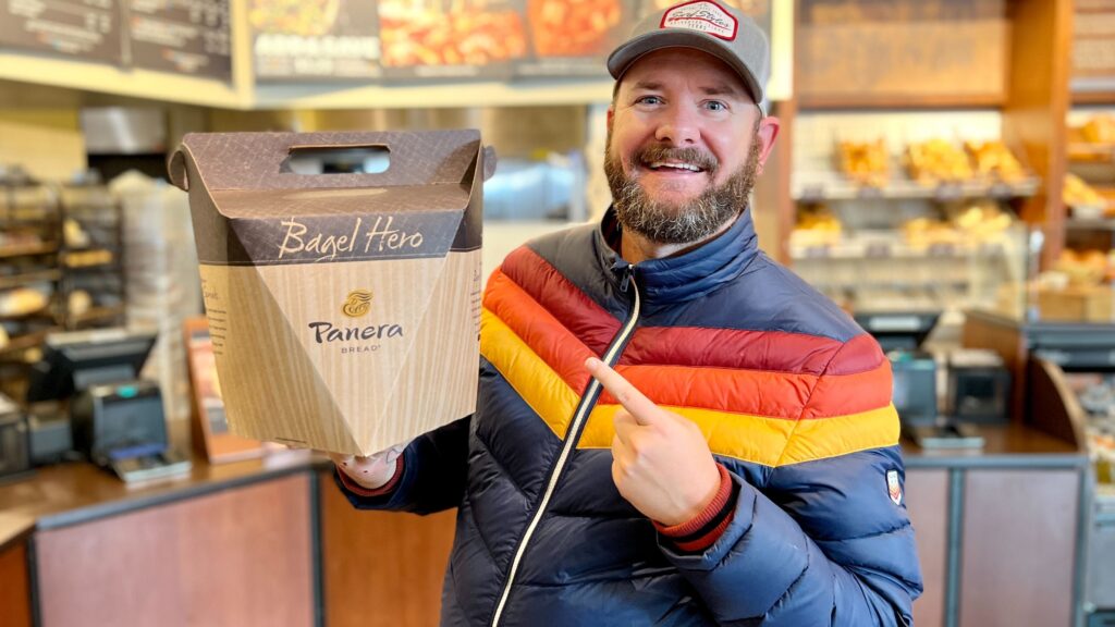 the freebie guy holding a box of bagels from panera in the panera store free food deals