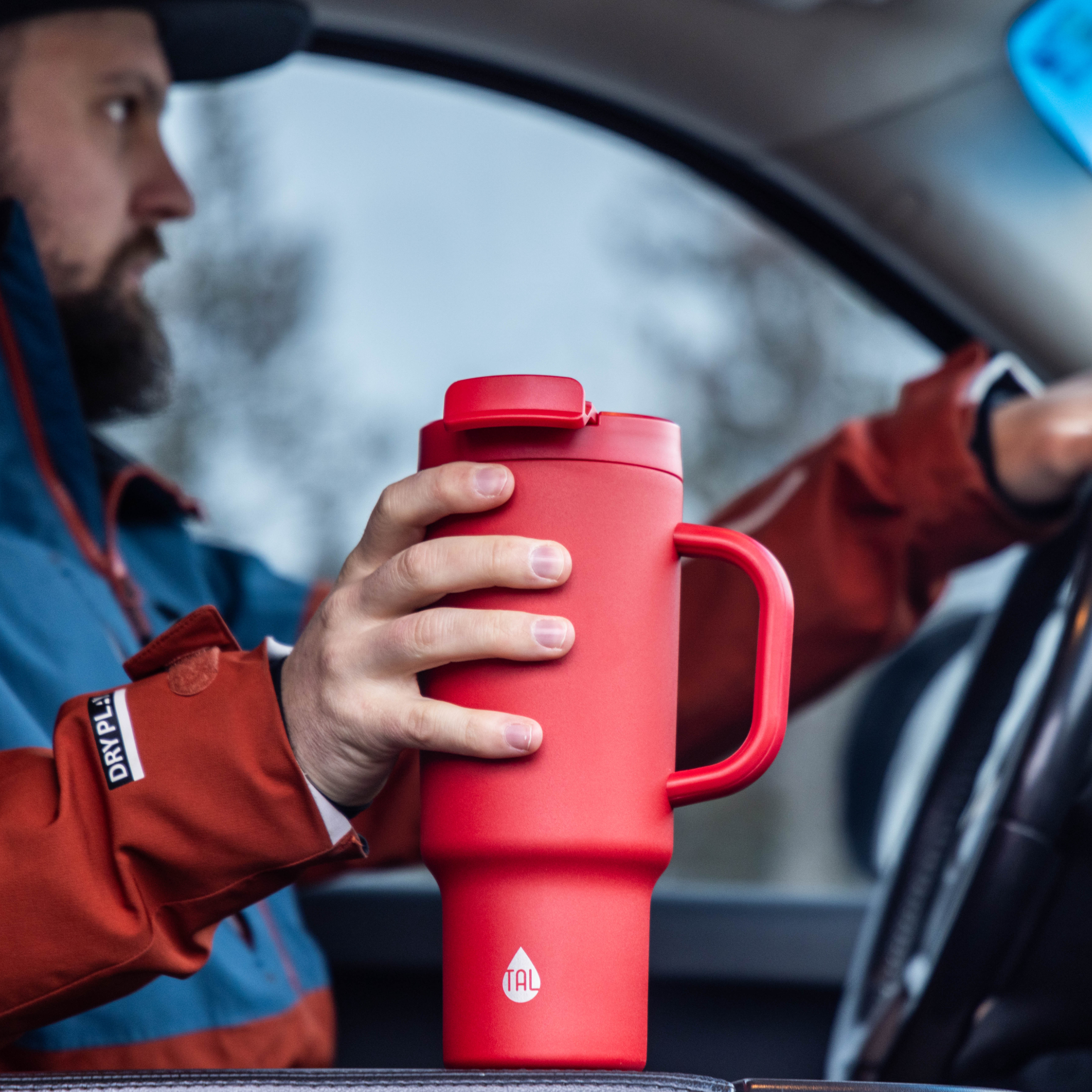 man driving a car and holding a red tumbler