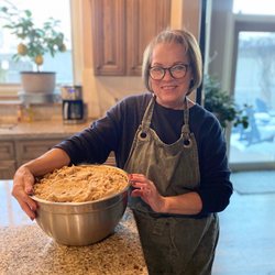 older lady in kitchen with apron on holding a mixing bowl
