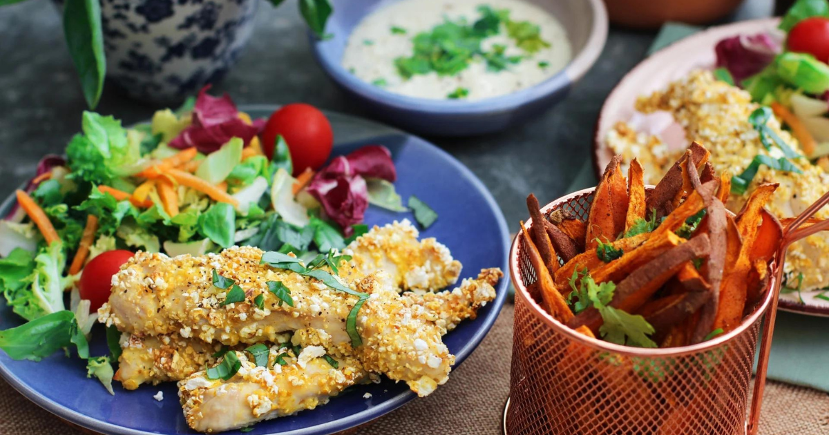 plated food on a table with a salad, chicken fingers, and a bowl of dip next to it