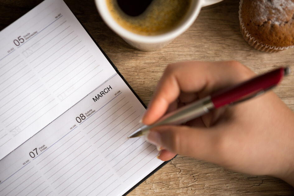 calendar laying on table hand with pen in it 