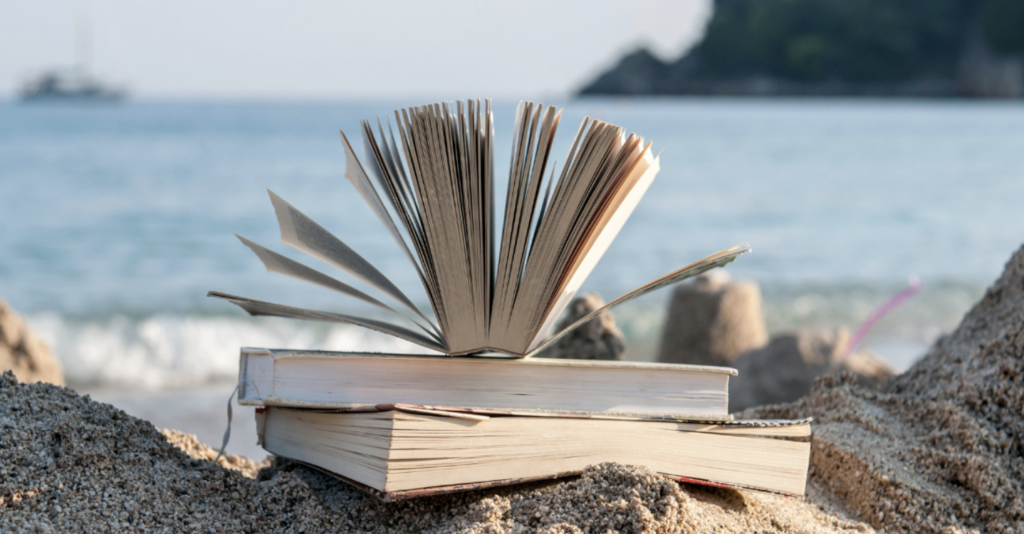 two books laying on the beach with a third book open on top