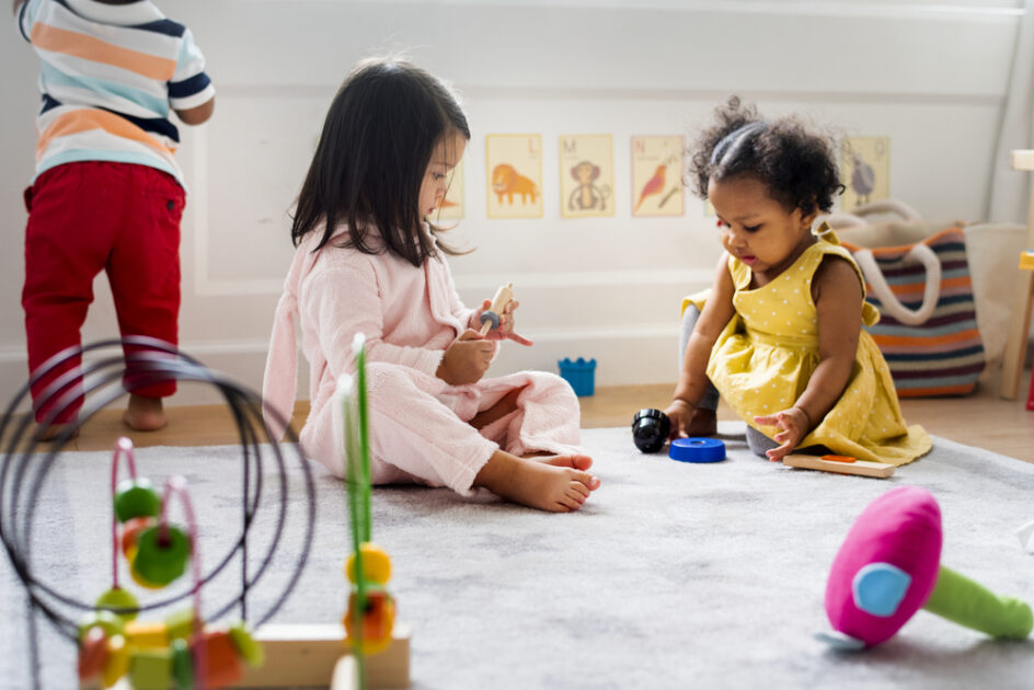 two toddler girls sitting on the floor playing with toys