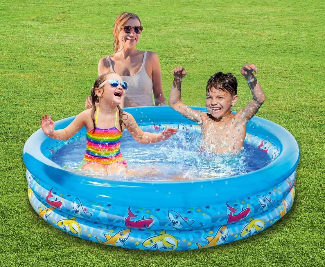 two kids playing in a pool and a woman sitting behind them