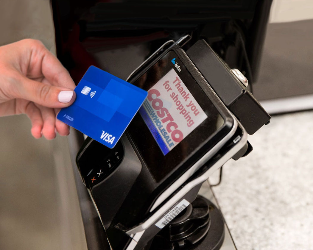 hand holding a credit card in front of a checkout at Costco