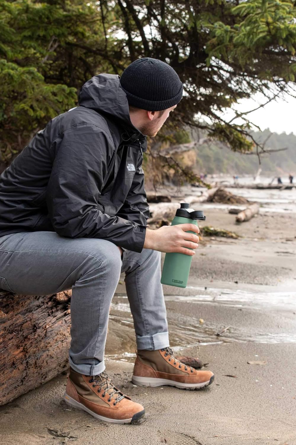 man sitting on a beach holding a Camelbak water bottle