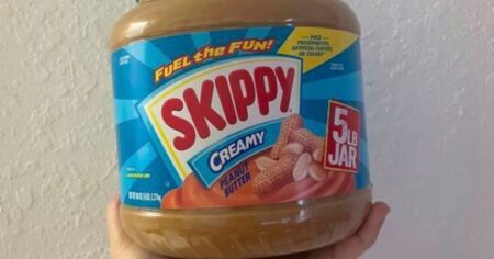 hand holding a big jar of peanut butter